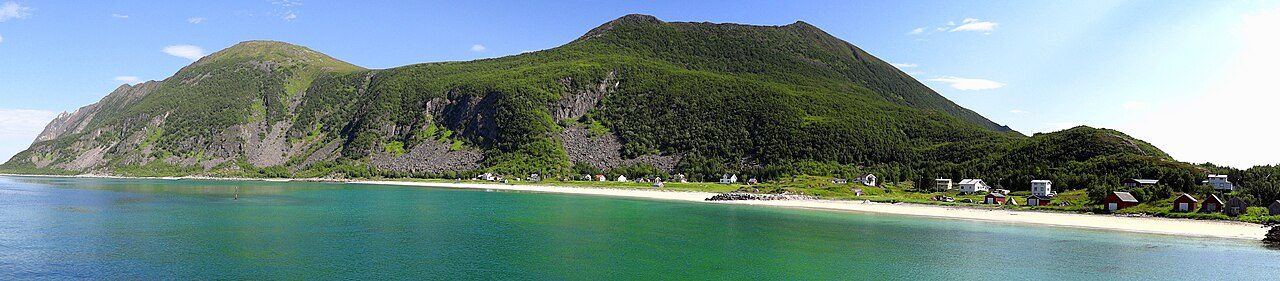 Lang hvit sandstrand ved Bøvær på ytre Senja, med fyrlykt og fjell i bakgrunnen