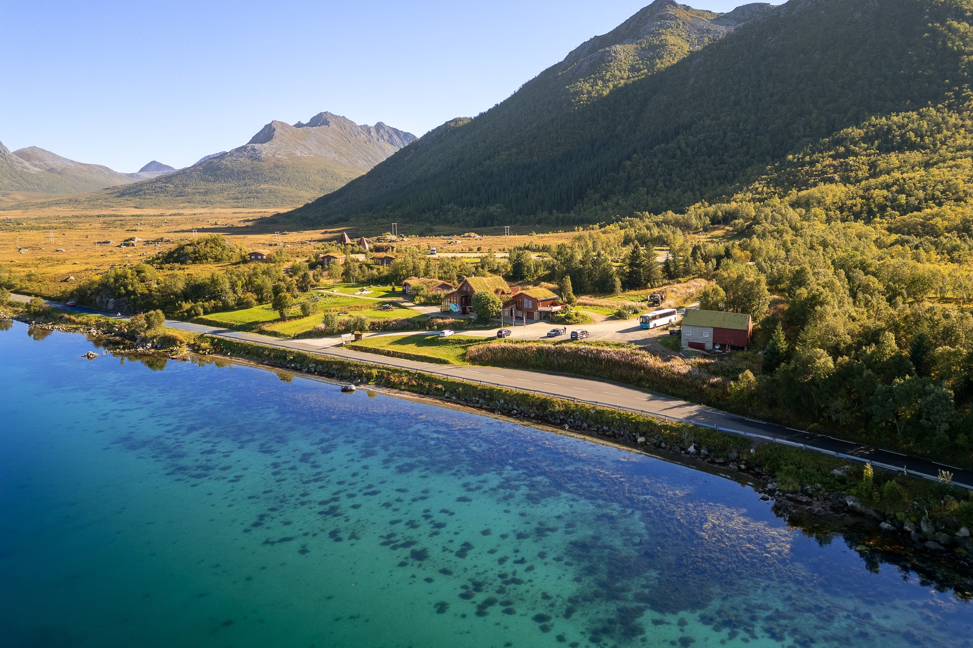 Drohnenaufnahme entlang der Rv82 beim Andøy Friluftssenter mit türkisblauem Fjord und steilen Bergen im Buksnesfjord