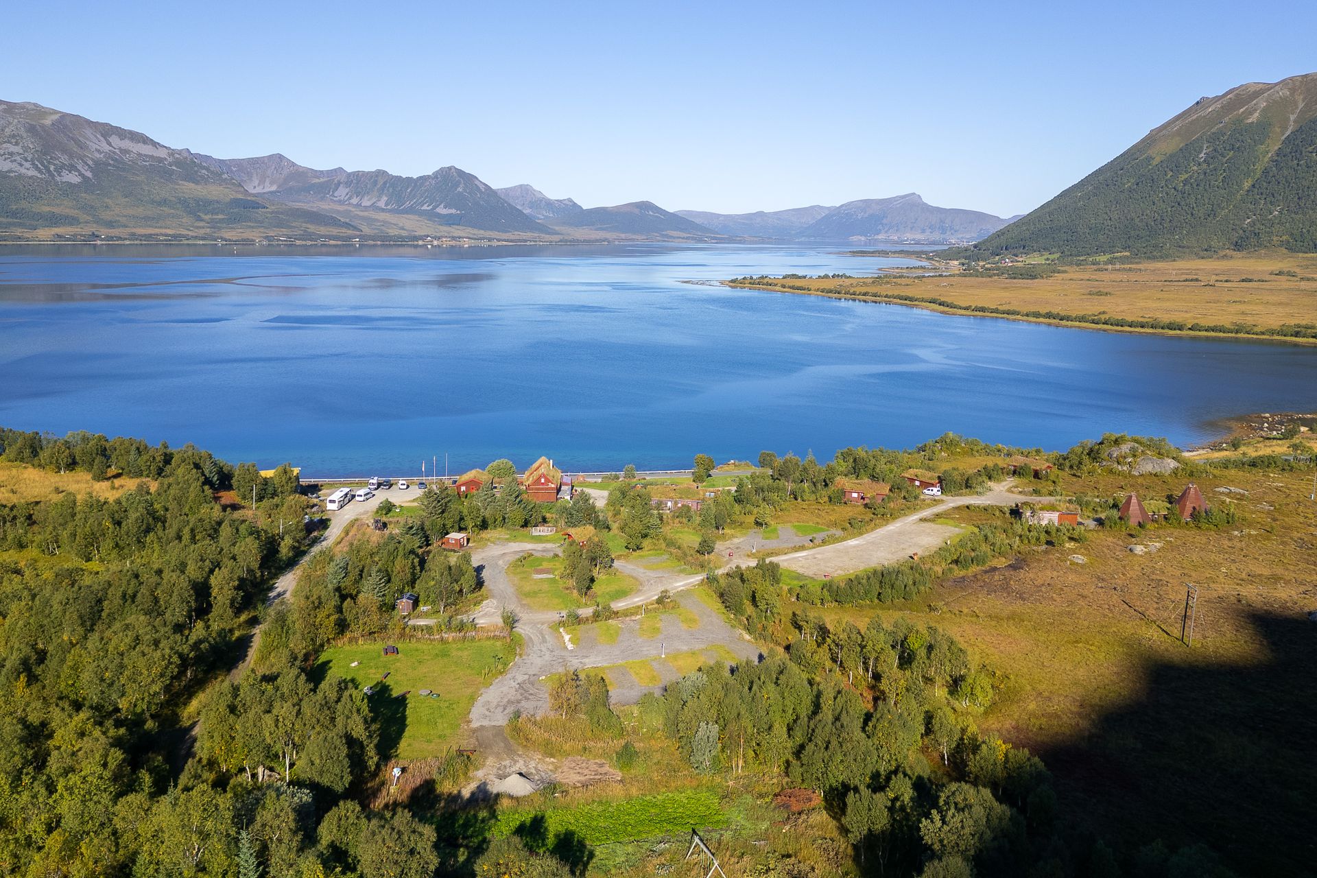 Dronefoto av Andøy Friluftssenter med oppstillingsplasser, bygninger og Buksnesfjorden omgitt av fjell
