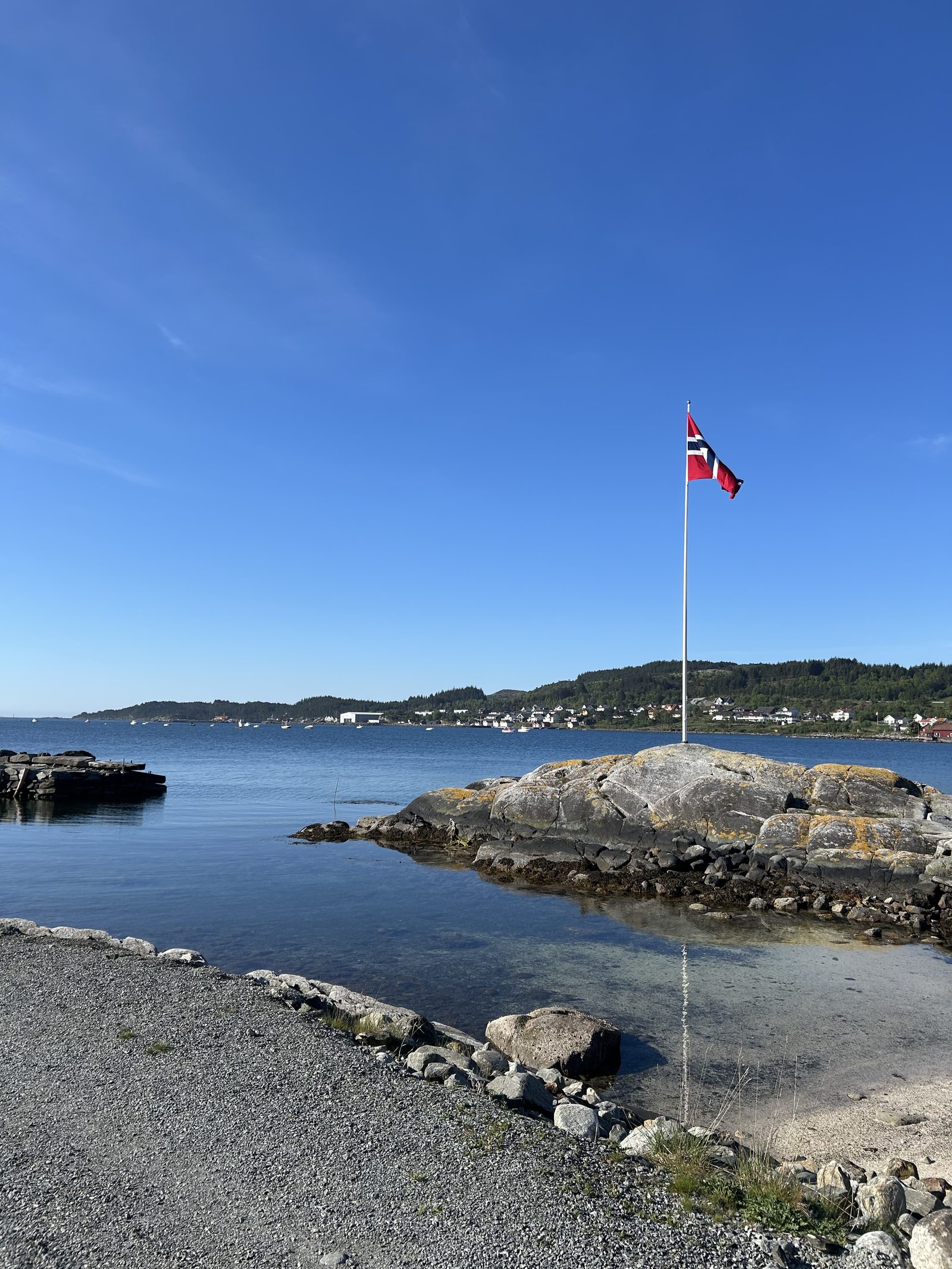 Norsk flagg på svaberg ved sjøen med kystlandskap og blå himmel over Boknasundet