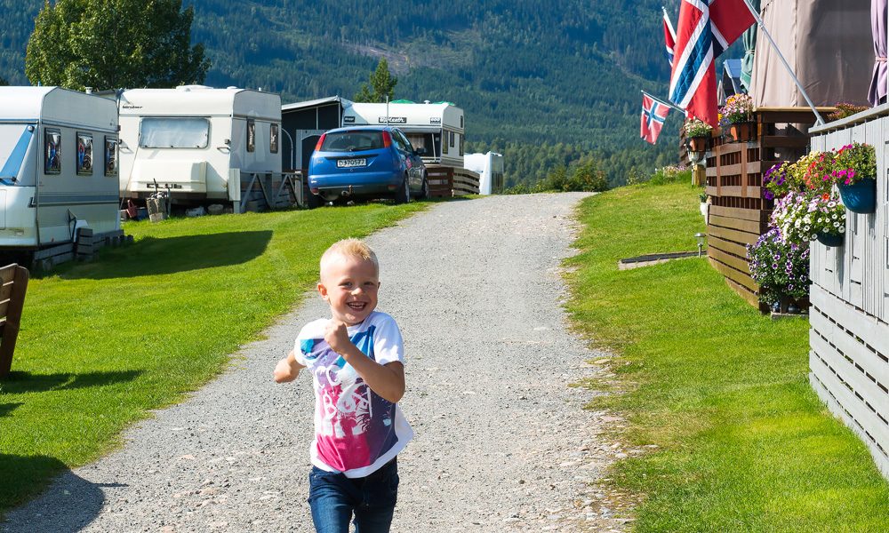 Campingplass ved bredden av Sperillen med sandstrand og bobiler, omgitt av skog i Ådal