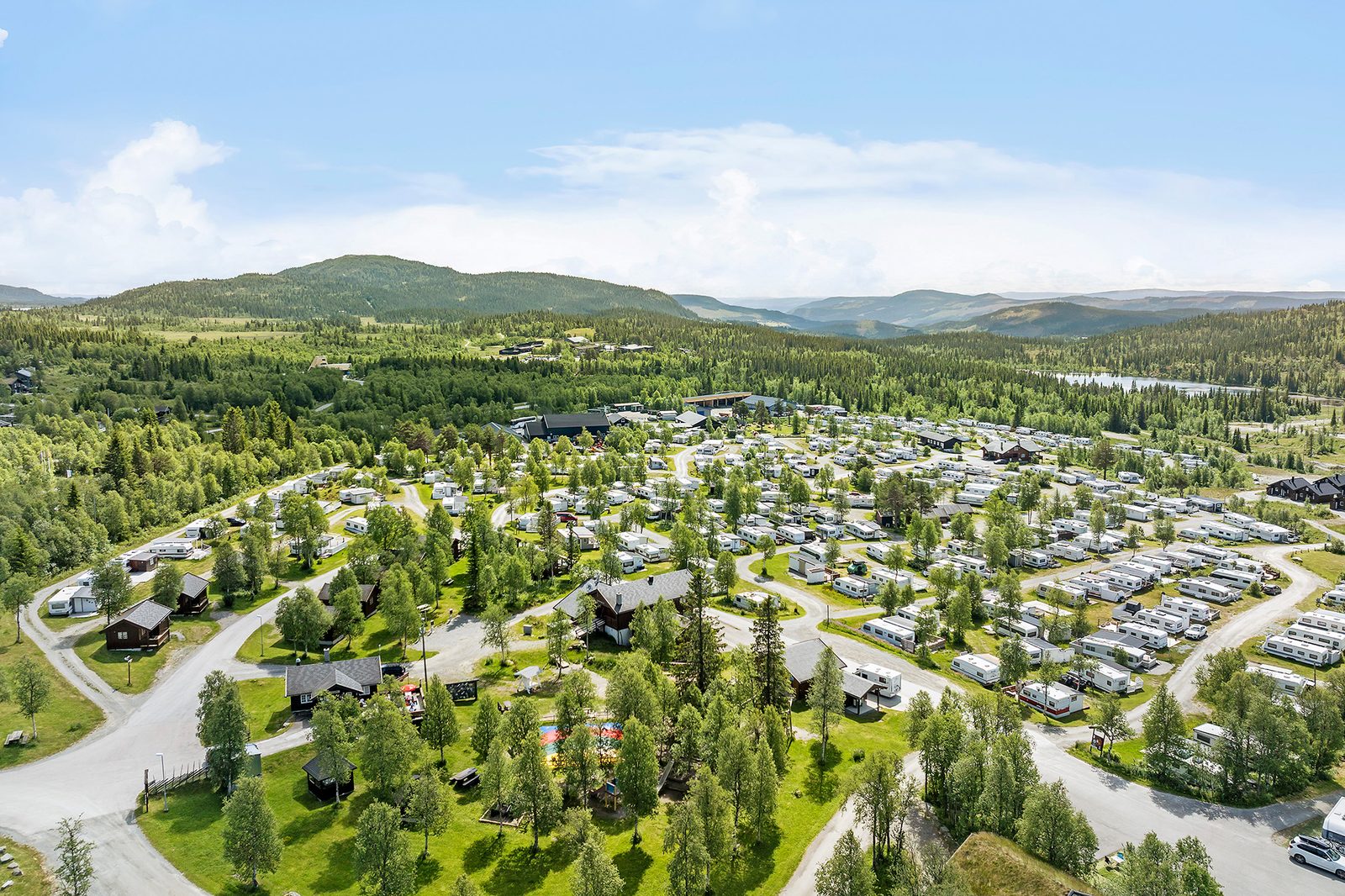 Bobiler og hytter på First Camp Beitostølen – Valdres med snødekte fjell i bakgrunnen