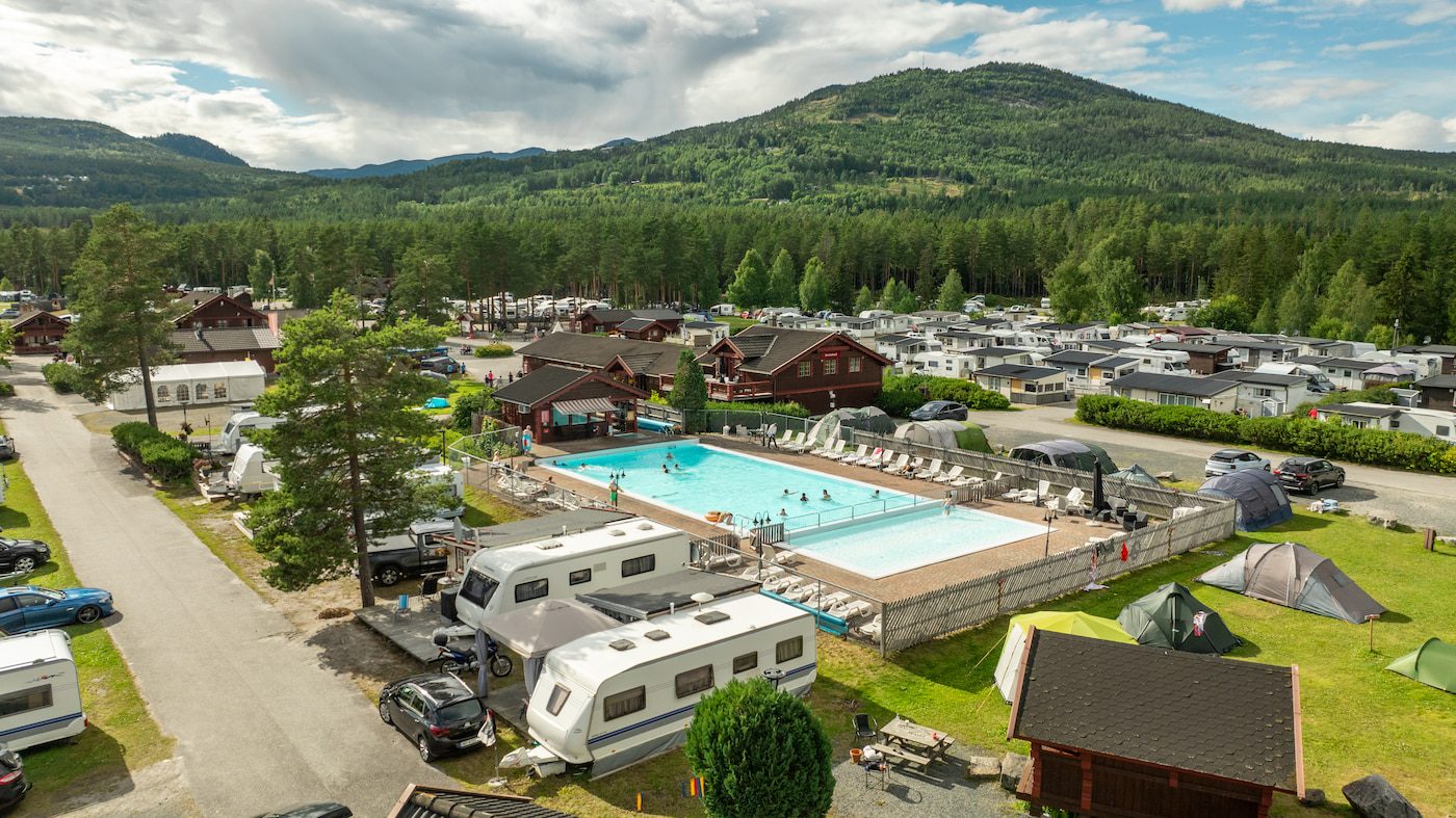 Bobiler, hytter og pods på First Camp Bø ved foten av Lifjell, med utendørsbasseng i forgrunnen og Bø Sommarland synlig i bakkant