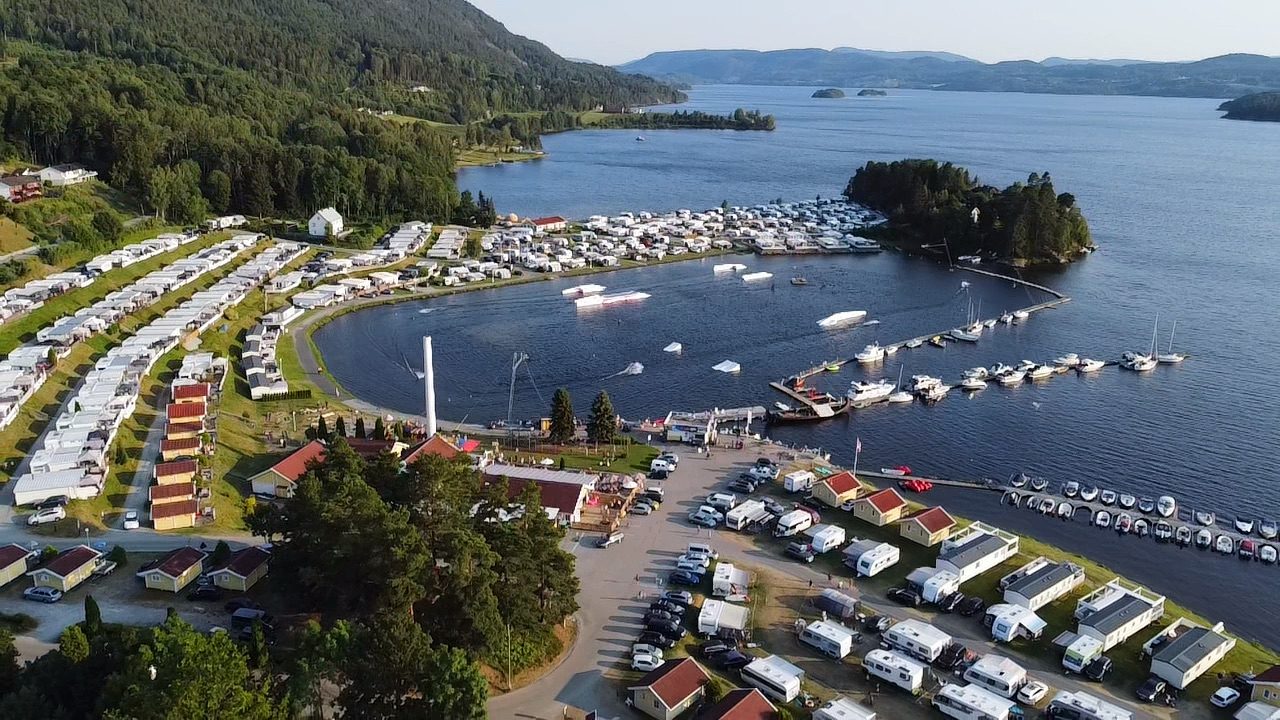 Bobiler og campingvogner på rekke ned mot Norsjø, med vannski-lift og badestrand i bakgrunnen