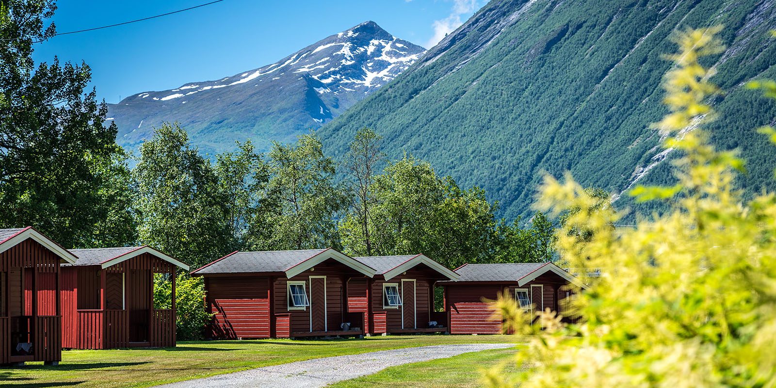 Campinghytter ved Valldalsvegen i Valldal, omgitt av frukthager og fjell i Fjord kommune