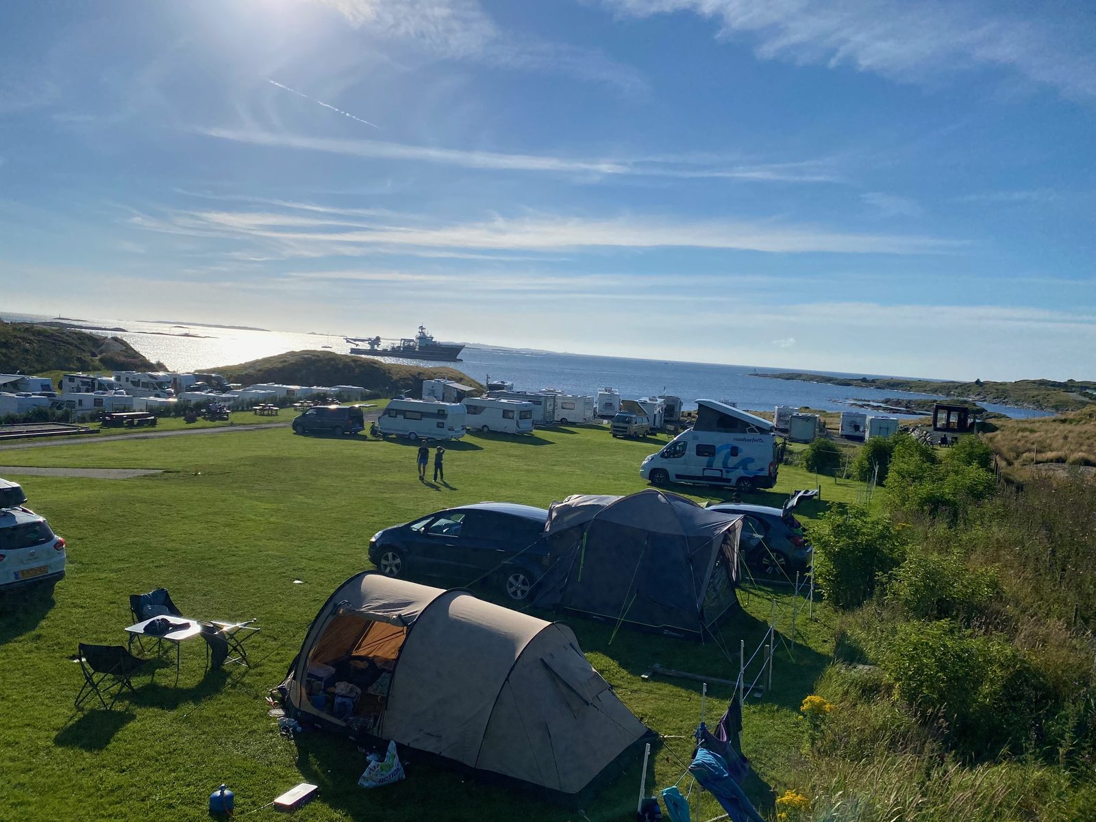 Telt, campingvogner og bobiler på gressplenen med skip og blå himmel over havet