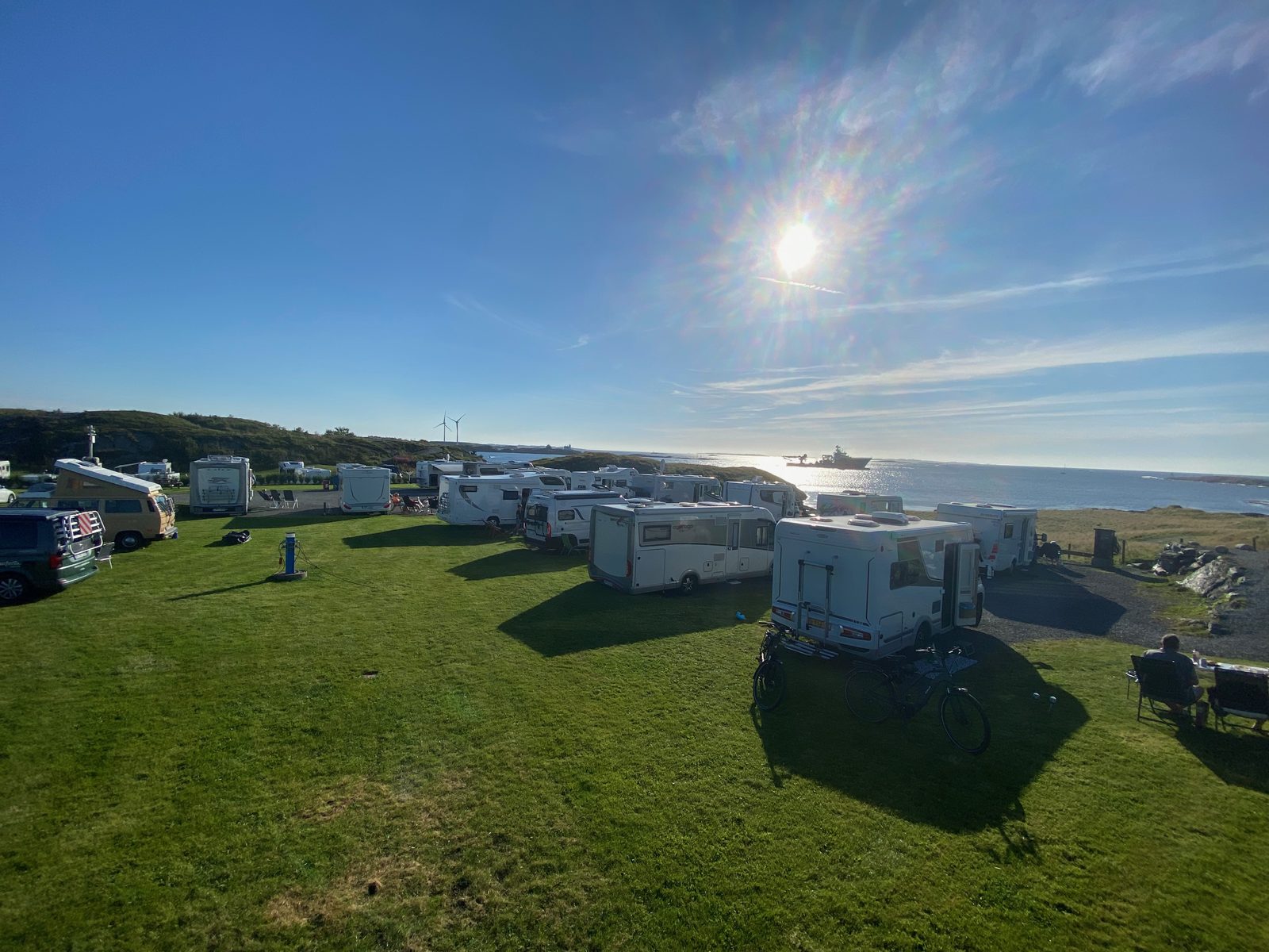 Bobiler oppstilt på gressplassen i sol med havet og vindmølle i bakgrunnen
