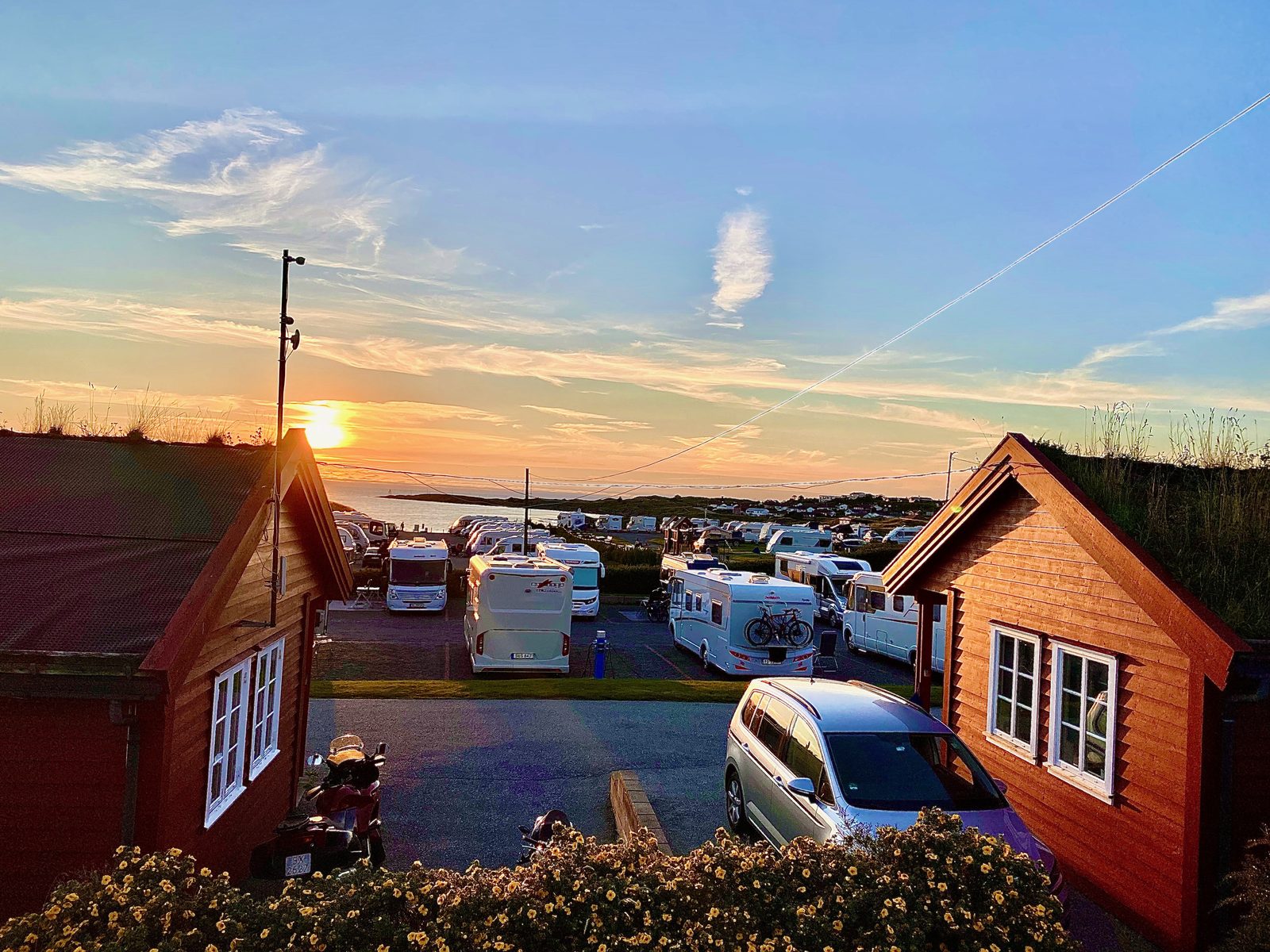 Solnedgang over havet bak utleiehytter med torvtak på Haraldshaugen Camping