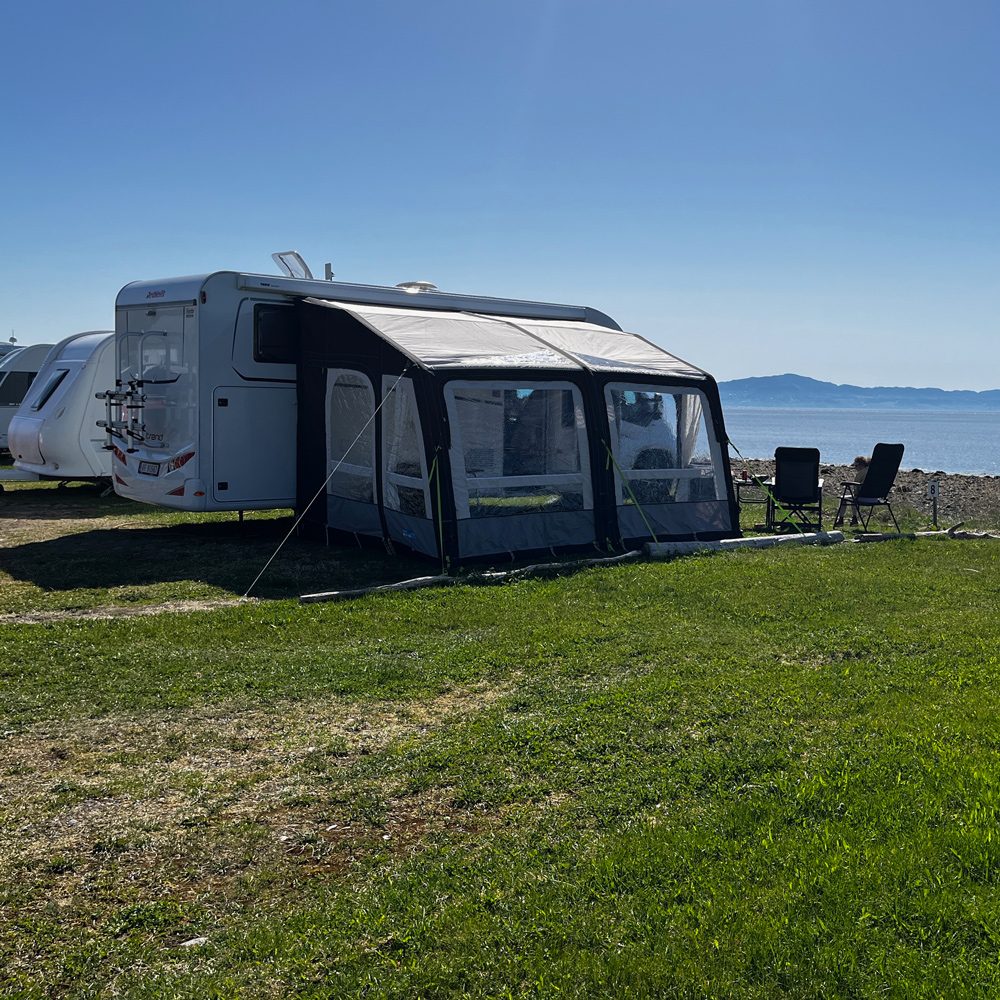 Bobiler og campingvogner på rekke ved sjøkanten på Hauganfjæra Camping med utsikt over Trondheimsfjorden