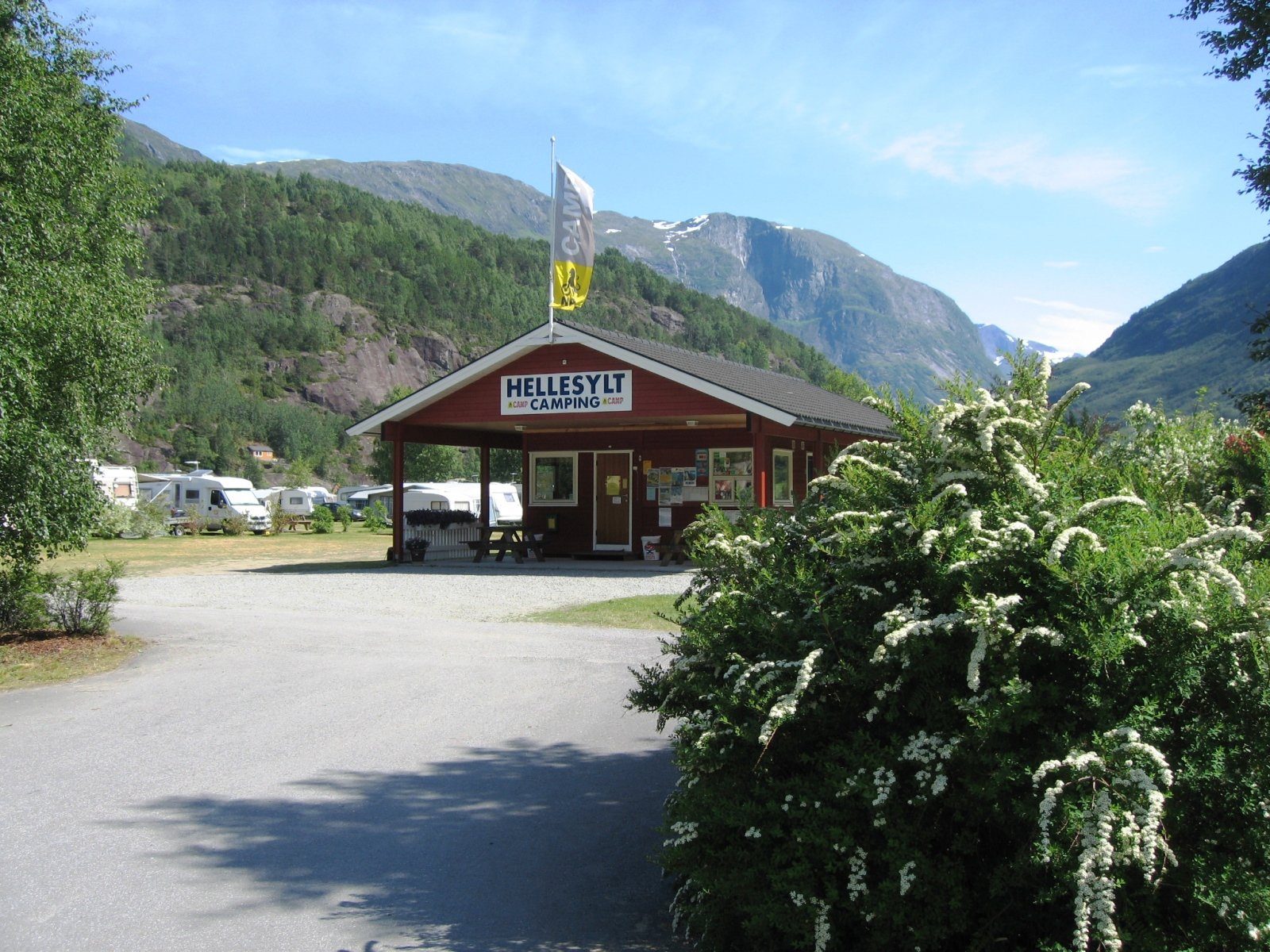 Bobiler og campingvogner på fjordnære oppstillingsplasser ved Storfjorden, med Hellesylt sentrum og bratte fjellsider i bakgrunnen