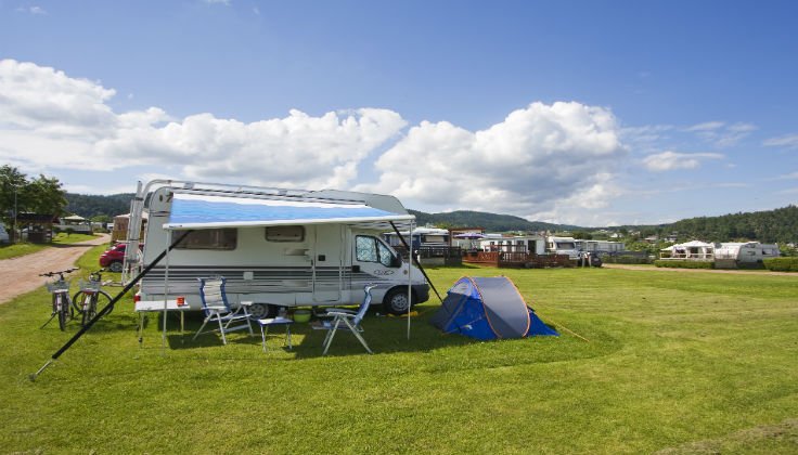 Bobil med utslått markise og blått kuppeltelt på gressplassen ved Homannsberget Camping med fjorden bak