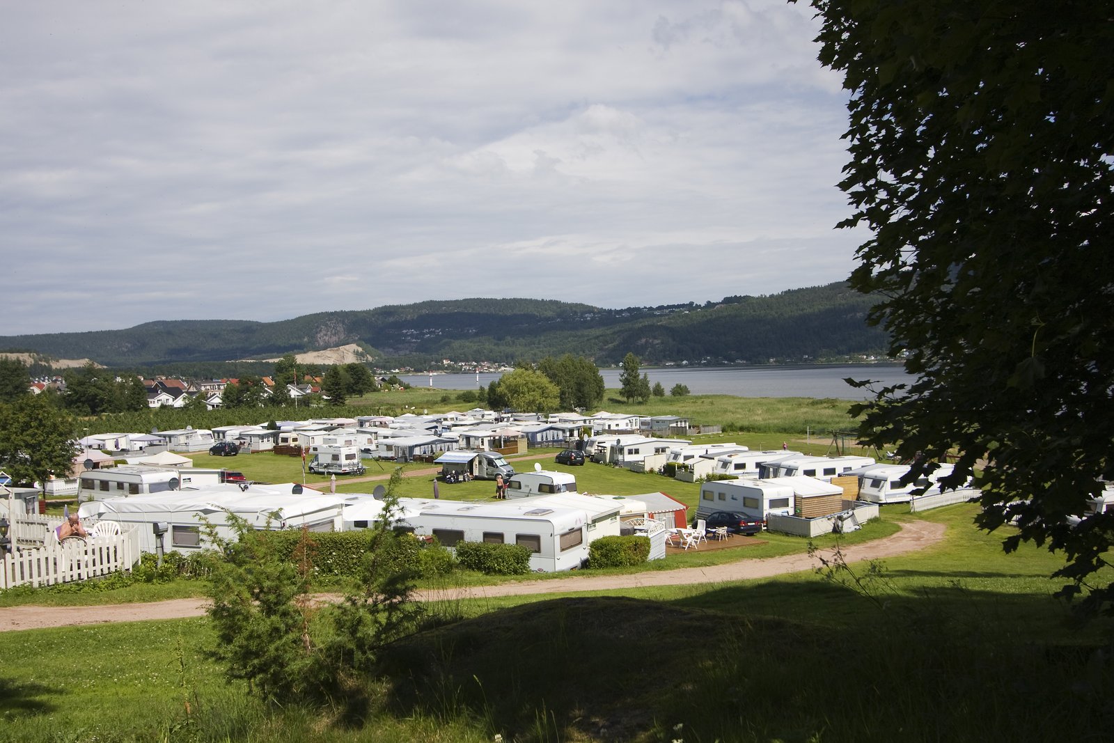 Oversiktsbilde over Homannsberget Camping med rader av campingvogner på grønt gress og Drammensfjorden i bakgrunnen