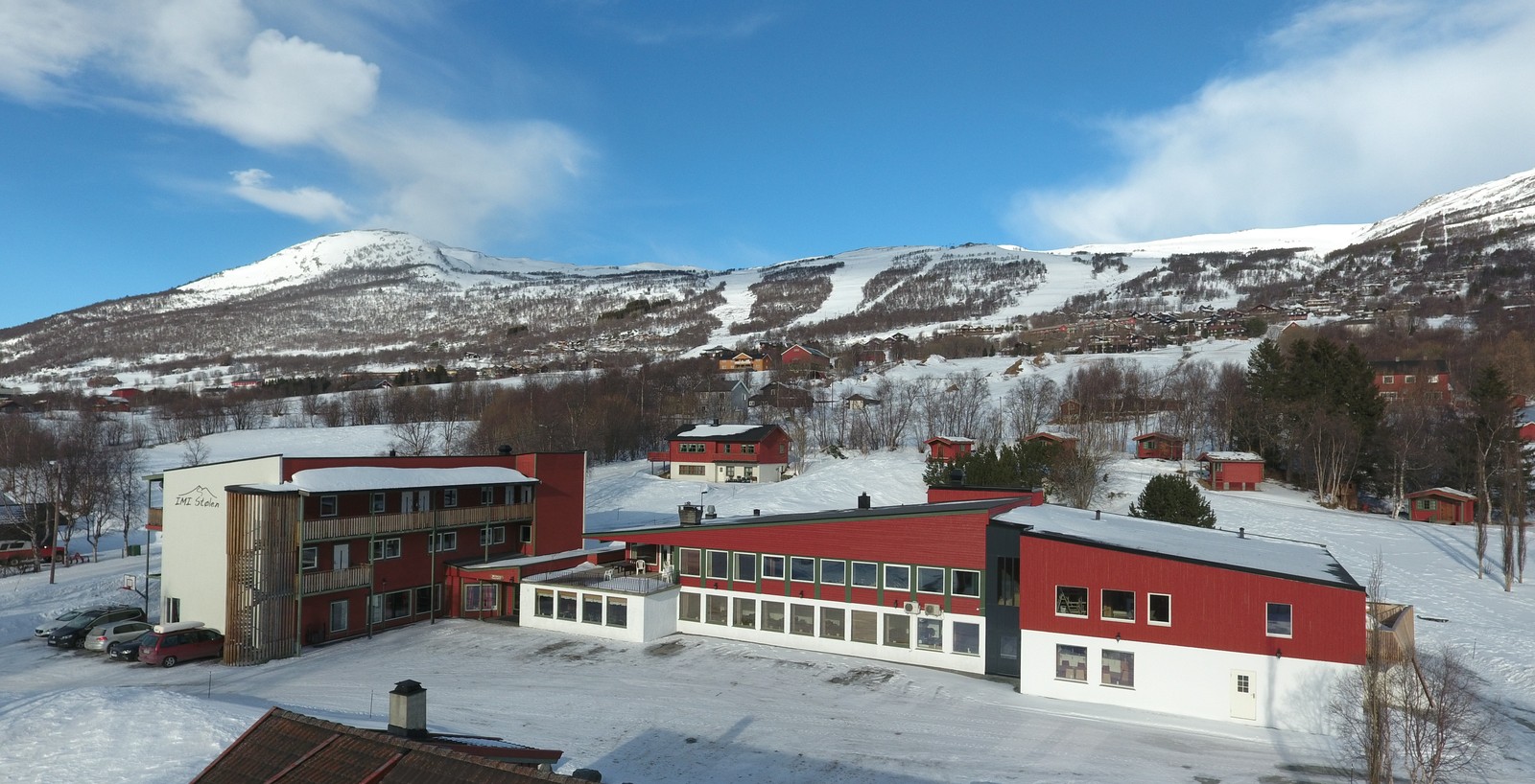 Vinterbilde av IMI Stølen med snødekte bygg og skibakkene i Stølenheisen bak