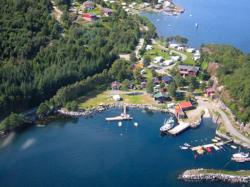 Magnillen Camping ved Tingvollfjorden med sandstrand, småbåthavn og hytter i bakgrunnen