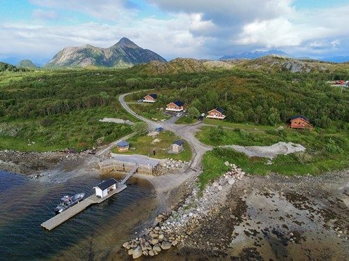 Sjønære utleiehytter ved kaia på Ytre Meløy med havet og Helgelandskysten i bakgrunnen