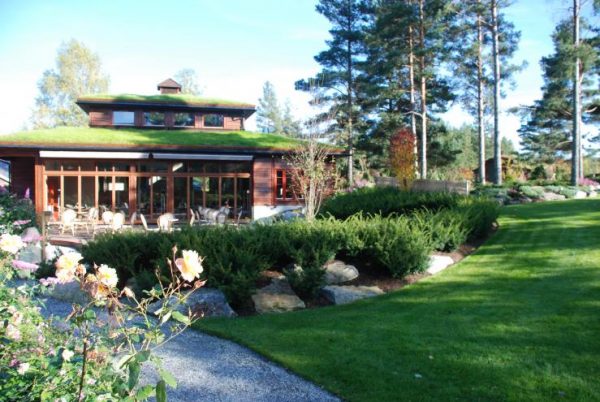 Bobil parkert ved Odden Camping ved elven Otra på Evje i Setesdalen, med Odden Hage og setesdalstilbygg i bakgrunnen