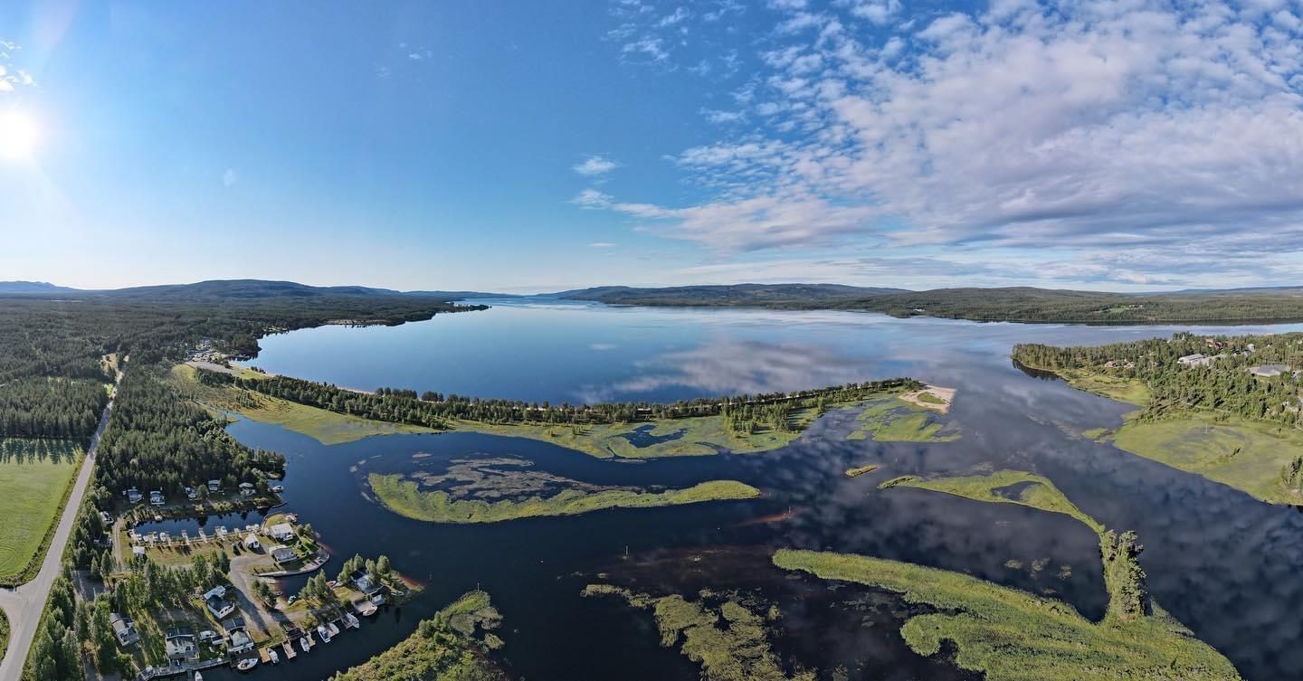 Den 1 km lange sandstranda ved Osensjøen Camping i nordenden av Osensjøen, med rolig vann og skogkledde åser i bakgrunnen