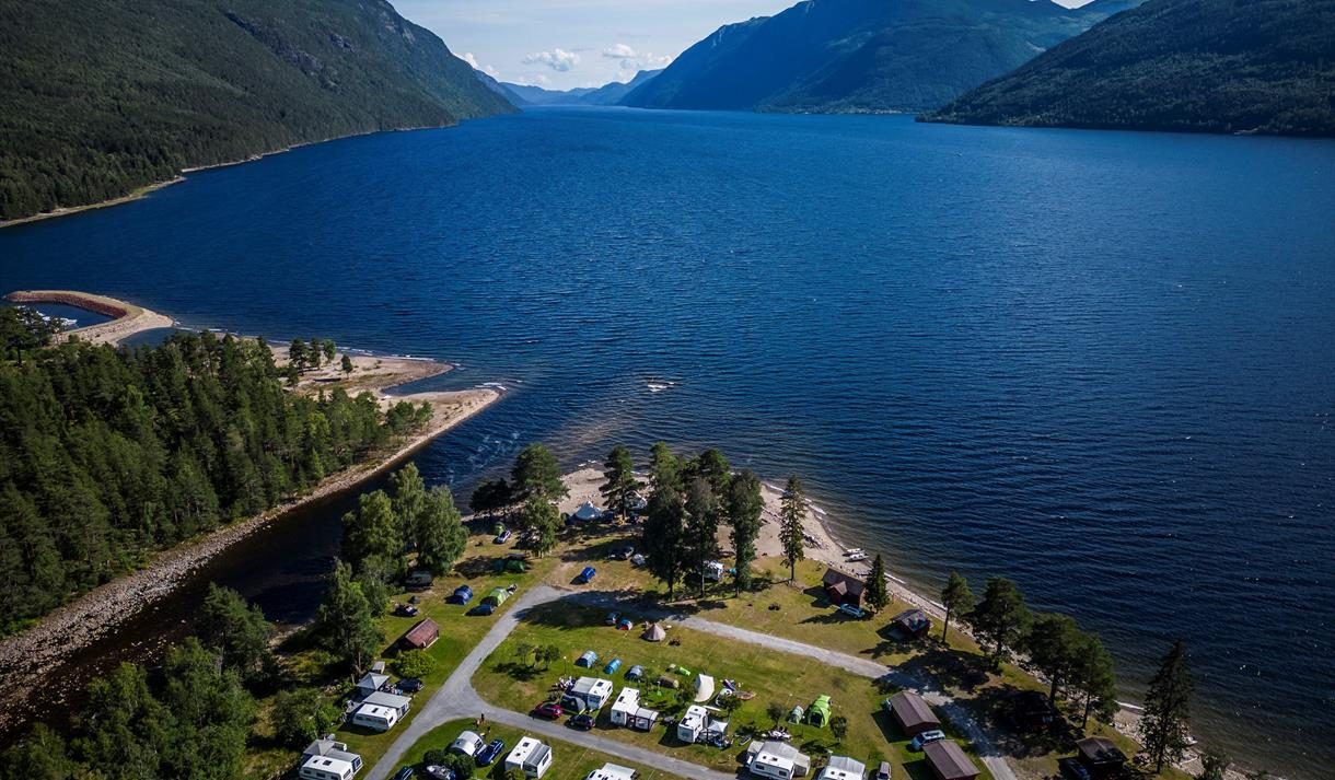 Hytter og campingvogner på grønn slette ned mot Tinnsjøen i Tinn Austbygd, med skogkledde åser i bakgrunnen