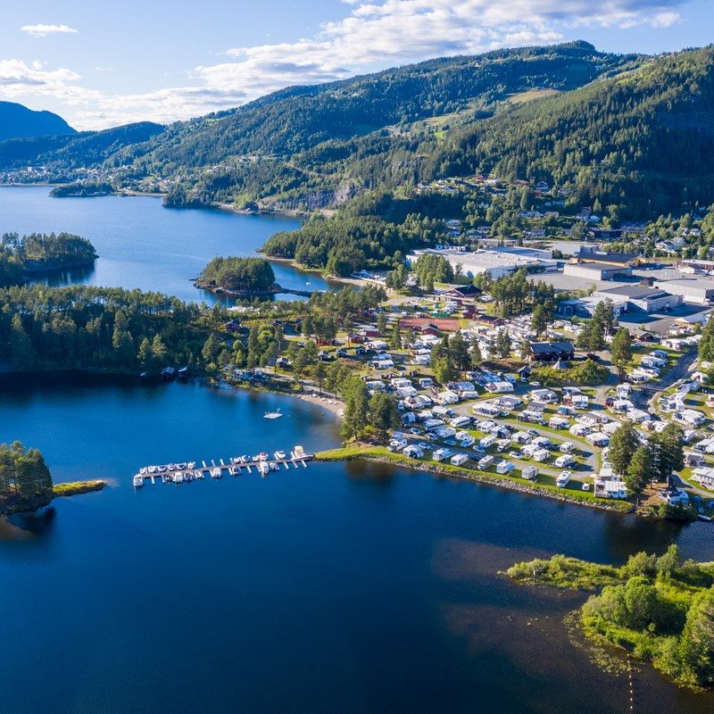 Flyfoto av Valdres Camping ved Strandefjorden, med campingplasser, hytter og fjorden i forgrunnen