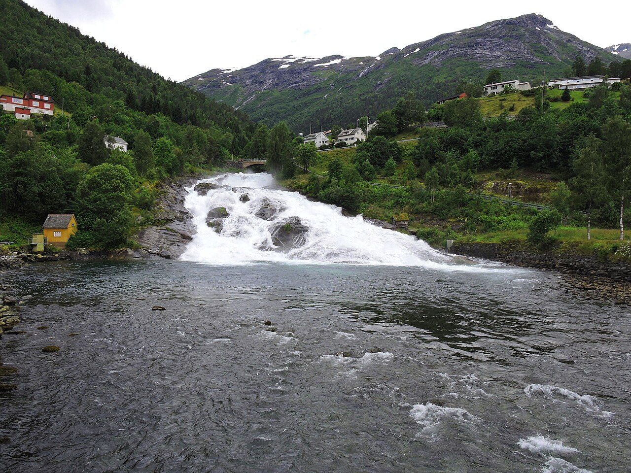 Hellesyltfossen stuper gjennom Hellesylt sentrum under historiske steinbroer mot Sunnylvsfjorden