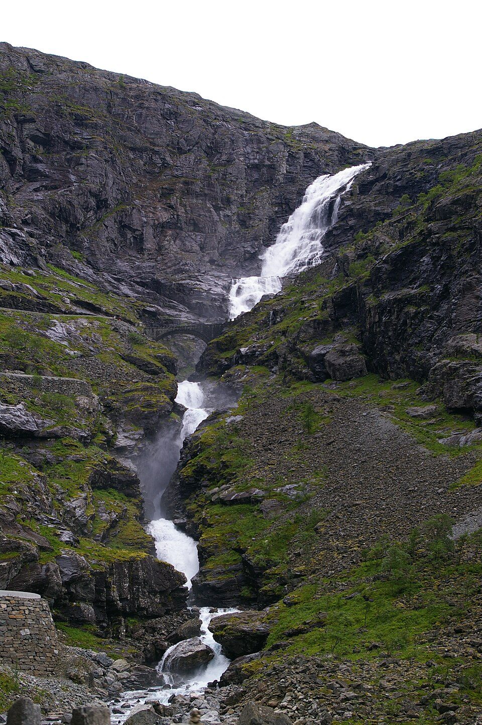 Stigfossen stuper 320 meter ned langs Trollstigens hårnålssvinger med Stigfossbrua i stein synlig i bakgrunnen