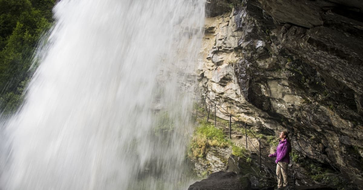 Storsæterfossen sett bakfra med vannmassene som styrter ned foran berghyllen og Geirangerfjorden i bakgrunnen