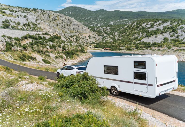 Adria Adora campingvogn på bergvei med bil foran og fjord i bakgrunnen