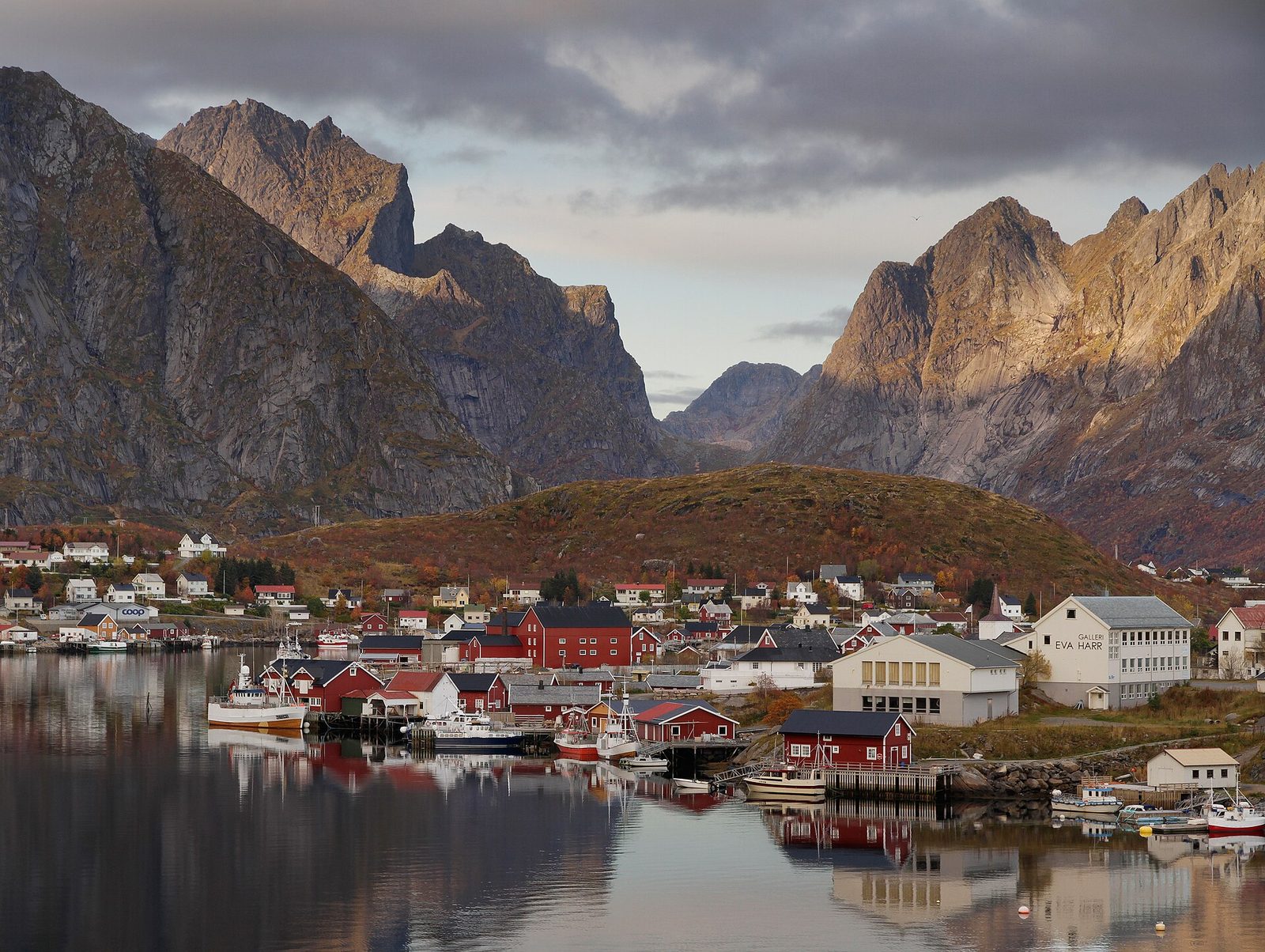 Reine i Lofoten med røde rorbuer og dramatiske fjell i bakgrunnen
