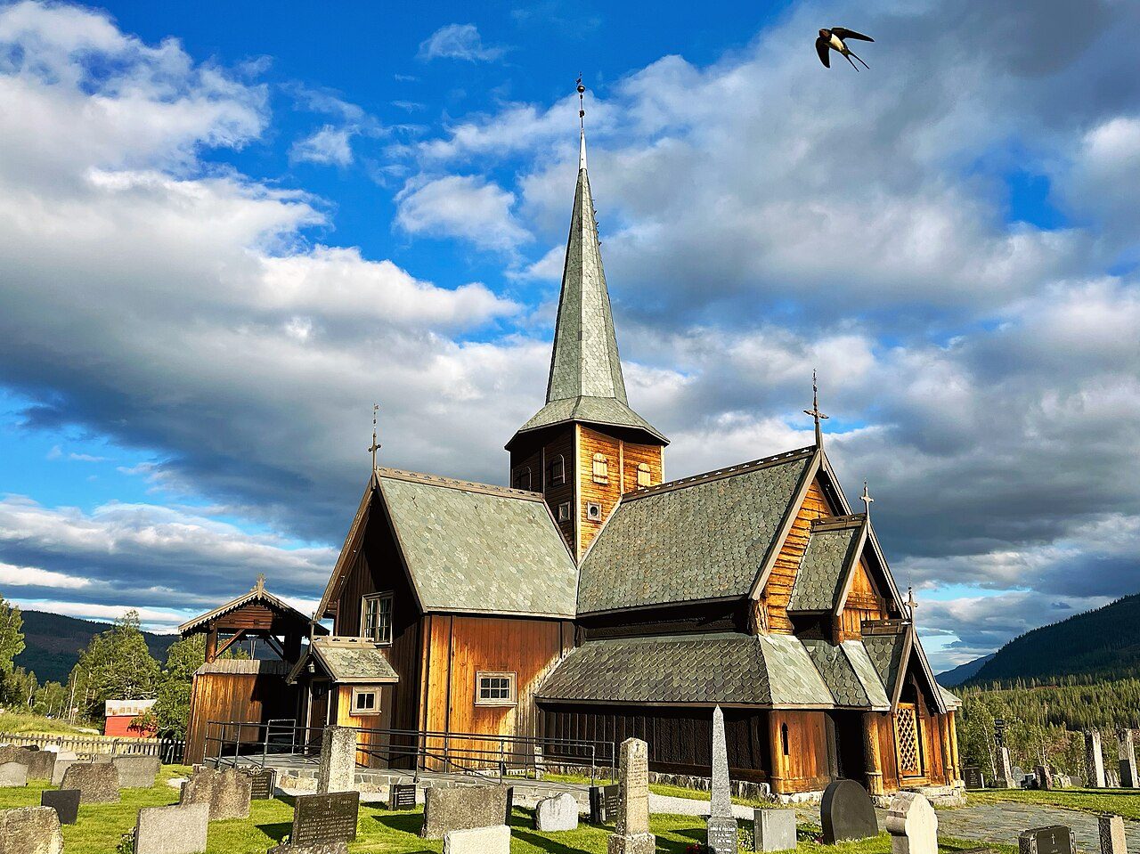 Hedalen stavkirke i Sør-Aurdal med spontak og hvitmalt kirkeskip omgitt av kirkegård