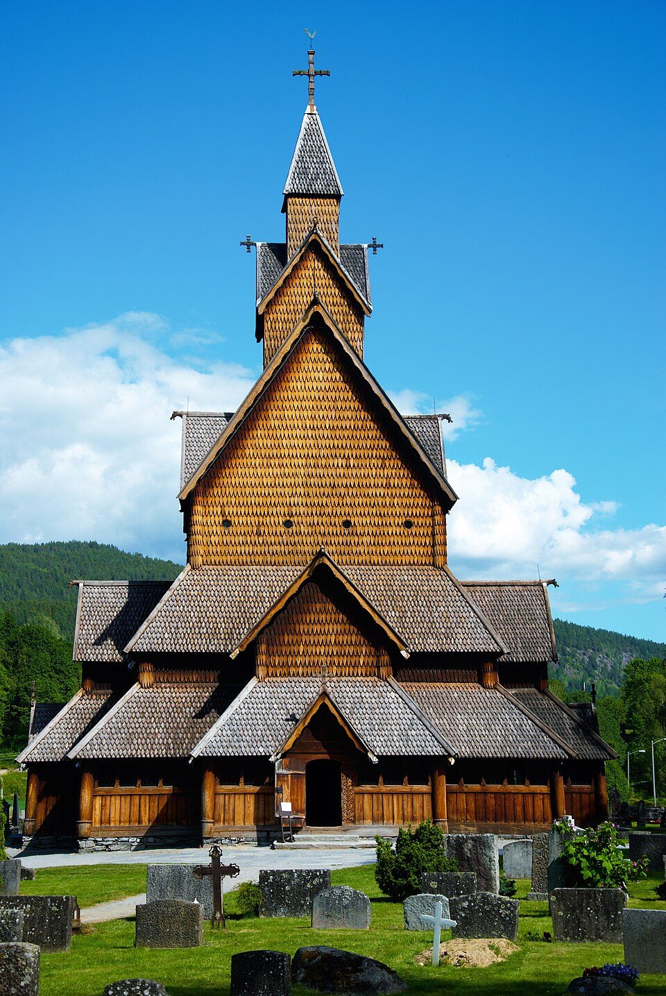 Heddal stavkirke i Telemark med tre tårn, takmøner og svalganger sett fra parkeringsplassen
