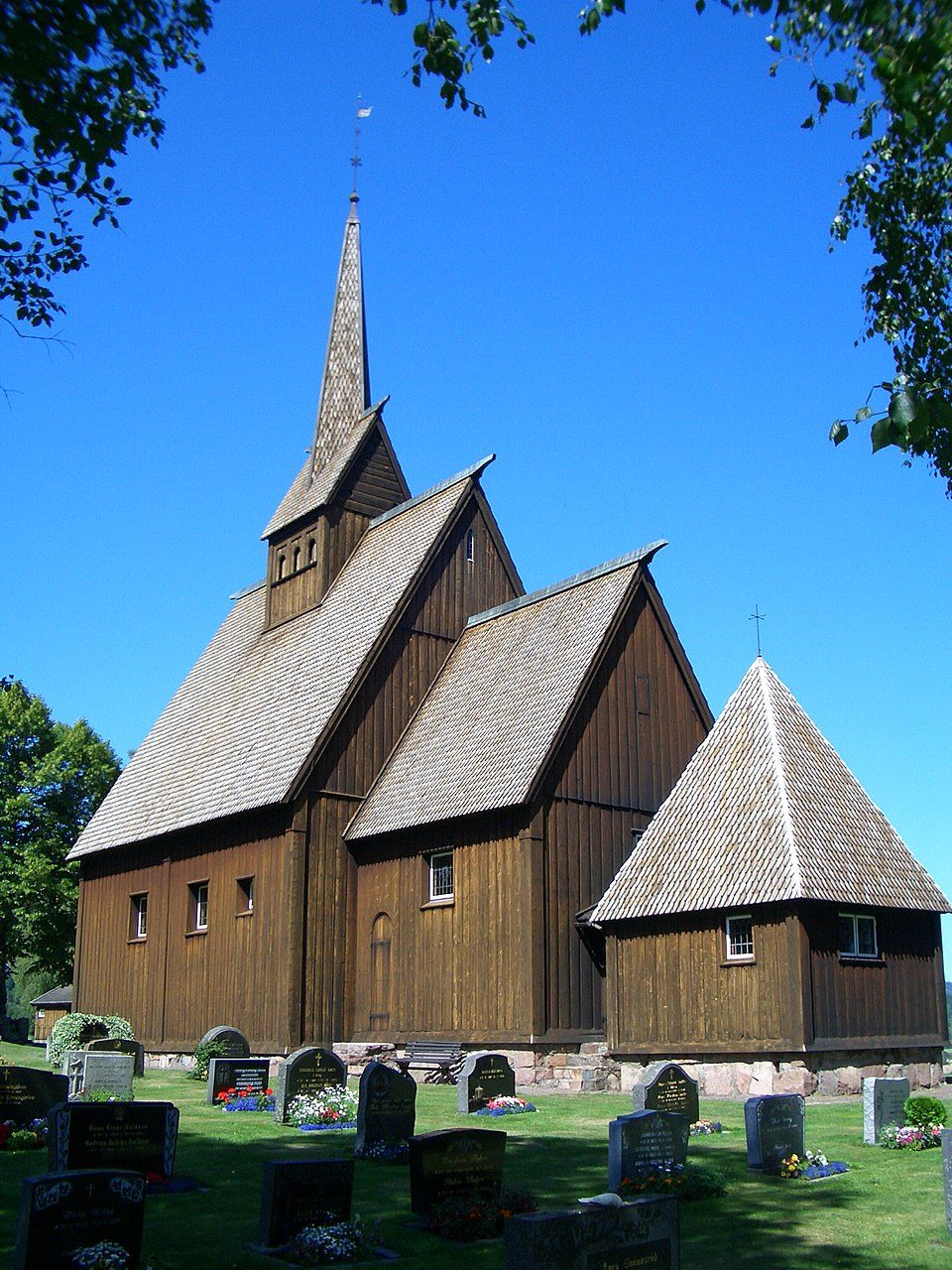 Høyjord stavkirke med tjærebredt tretak og spir i landlig vestfoldlandskap