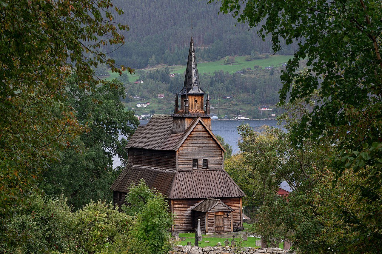 Kaupanger stavkirke med tjærebredd langside og hvit takrytter mot grønne marker ved Sognefjorden