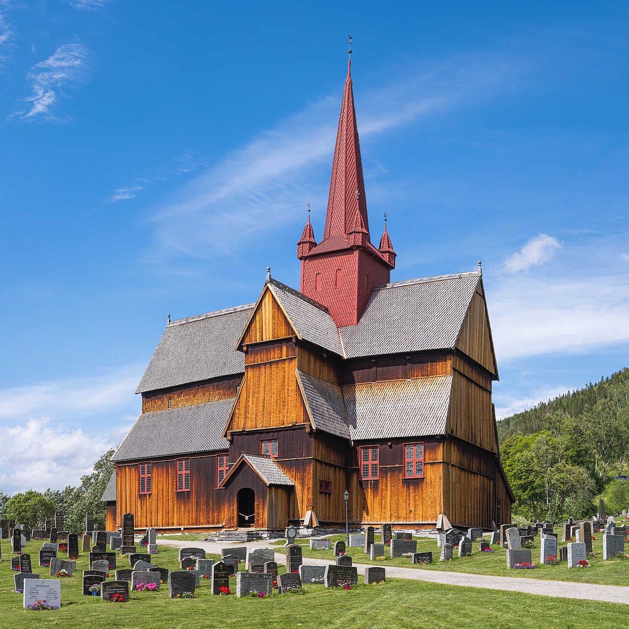 Ringebu stavkirke med karakteristisk rødt tårn og korsformet skip mot grønt landskap i Gudbrandsdalen