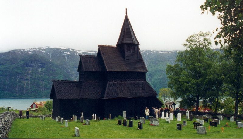 Urnes stavkirke i tre med tjærebredde vegger og spisse takflater over Lustrafjorden